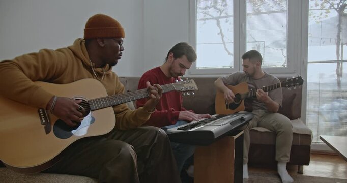 Three friends gather in their living room, enjoying a jam session with acoustic and electronic instruments. The diverse trio creates music together, showcasing creativity and camaraderie.