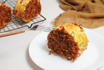 A savory meat floss bread roll topped with sesame seeds and sliced chilies is lifted with a fork. The soft texture and rich filling are clearly visible in this close-up shot.