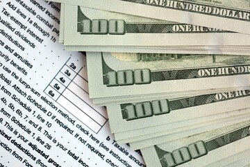 Big amount of United States hundred dollar bills in bunch on table with tax return form