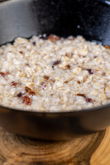porridge with dried fruits in a black bowl , cooking instant oatmeal porridge, close up, side view
