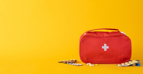 Red first aid kit positioned on a vivid yellow background with spilled pharmaceuticals, symbolizing...
