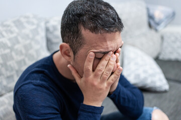 Depressed man sitting on sofa covering face with hands