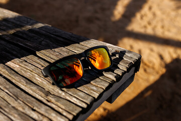 Sunglasses with protective lenses in yellow and orange colors laying on a wooden table on the beach...