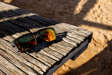 Sunglasses with protective lenses in yellow and orange colors laying on a wooden table on the beach...