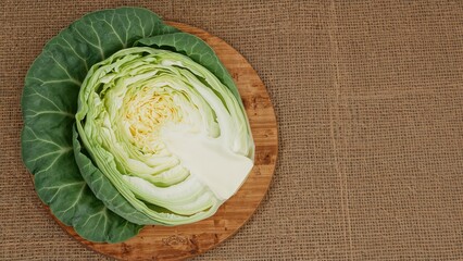 Green cabbage resting on a wooden surface with burlap backdrop