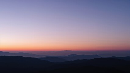 Obraz premium Silhouetted mountain ridges beneath a calm twilight sky glowing with purple and pink colors