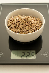 Black scales on white canvas background with bowl with sunflower seeds, showing 225 grams. Selective focus. Vertical shot.
