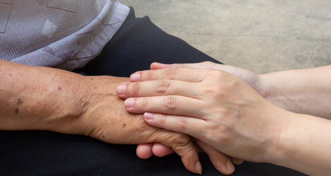 Elderly female hand holding hand of young caregiver at nursing home.Geriatric doctor or geriatrician concept. Doctor physician hand on happy elderly senior patient to comfort in hospital examination