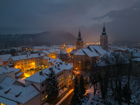 Aerial view of snow-dusted rooftops and the illuminated spires of the Church of St. Francis Xavier pierce the twilight sky, Bansk&Atilde;&iexcl; Bystrica, Banskobystrick&Atilde;&frac12; kraj, Slovakia.