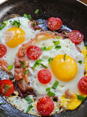 Fried eggs with bacon and tomatoes on a wooden table