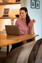 Happy woman using laptop at home and celebrating her success