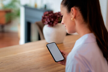 Close-up of a woman sitting at a table and using a blank screen smart phone