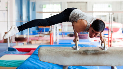 Young man performing gymnastic elements on pommel horse