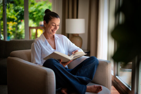 Smiling middle aged woman relaxing at home and reading a book