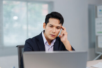Asian businessman suffering from headache, massaging his temple, looking at laptop screen, having...