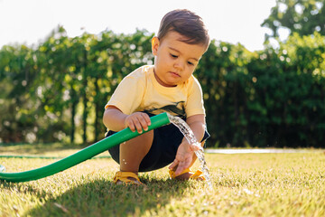Curious toddler playing with water from a garden hose on a sunny day