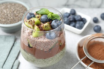 Delicious chocolate pudding with chia seeds, kiwi, mint and blueberries in glass on grey table,...