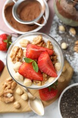 Delicious chocolate pudding with chia seeds, strawberries, yogurt and nuts in glass on white table, flat lay