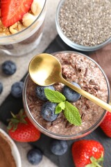 Delicious chocolate pudding with chia seeds, strawberries and blueberries in glass on light grey table, flat lay
