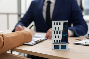 Real estate agent working with client at desk in office, focus on house model