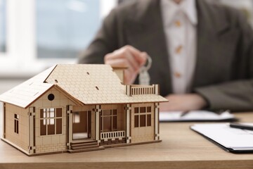Real estate agent holding key at desk in office, focus on house model