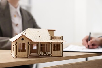 Real estate agent working with client at desk in office, focus on house model