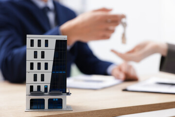 Real estate agent giving key to client at desk in office, focus on house model