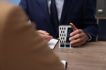 Real estate agent working with client at desk with house model in office, closeup
