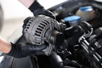 Obraz premium Auto part. Professional mechanic with alternator near open hood of car indoors, closeup