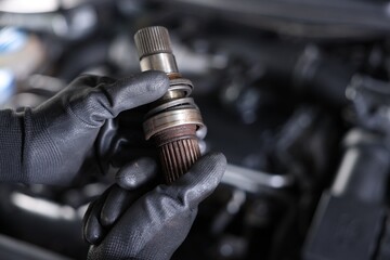 Auto part. Professional mechanic with drive shaft near open hood of car indoors, closeup. Space for...