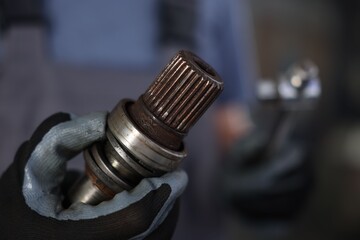 Auto part. Professional mechanic with drive shaft and tool indoors, closeup. Space for text