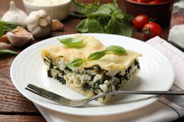 Piece of tasty vegetarian lasagna and ingredients on wooden table, closeup