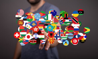A man interacts with a digital display of flags representing countries worldwide.  Global business,...
