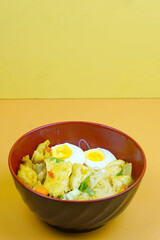 A vibrant bowl of Bihun Kari or Indonesian curry vermicelli noodles, chicken, eggs, and vegetables in a rich yellow broth.