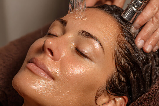 Close-up of a woman receiving a head massage during a Japanese head spa treatment with water flowing from a special hair washing tool, focusing on the scalp relaxation and beauty therapy