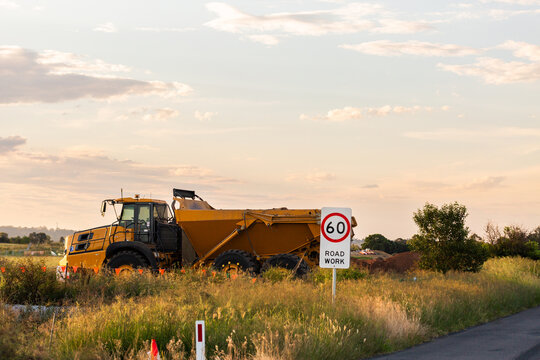 pastel sky over dump truck beside road works 60 speed limit sign on roadside