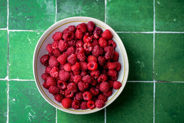 Plate of freshly picked red raspberries on green tile background. Concept of vibrant colors, summer, harvest, healthy organic food.