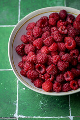 Plate of freshly picked red raspberries on green tile background. Concept of vibrant colors, summer, harvest, healthy organic food.