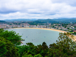 Fototapeta premium La Concha Bay in San Sebastián, Spain, viewed from Mount Igueldo—panoramic coastal scenery with sandy beach, boats, and cityscape under a dramatic sky, perfect for travel and vacation imagery.