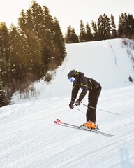 Young male skier training in black outfit pants jumps off freestyle on snowy slope mid-air trick...