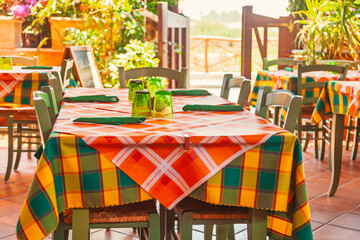 Colorful outdoor restaurant tables with checkered tablecloths and green glasses in Mediterranean setting