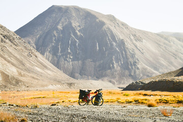 Red touring bicycle loaded with heavy gear in four pannier bags stand on side of gravel road...