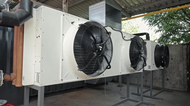 Industrial HVAC condenser units with ventilation fans. Large commercial HVAC condenser units equipped with powerful ventilation fans, installed in a covered outdoor space for climate control.