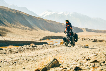 Male solo cyclist bicycle touring in remote mountains sunny outdoors enjoy panorama outdoors fresh air asia travel. Bartang valley. Tajikistan. Silk road Europe to asia famous travel destination