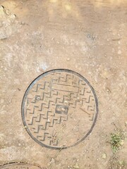 Manhole Cover on Dirt Ground with Geometric Pattern
