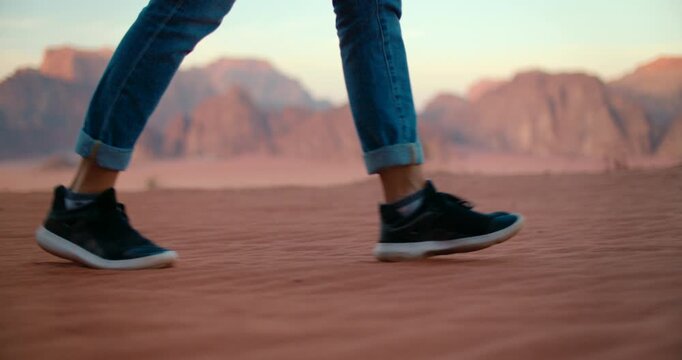 Slender female feet in sporty shoes walking on red sand in Wadi Rum Desert in Jordan. Middle Eastern adventure and outdoor spirit with steps of unrecognizable woman. 4K Close-up slow motion shot 