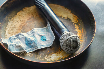 Microphone and dollar bill on a dirty old frying pan close-up, journalistic ethics, fake news, fact...
