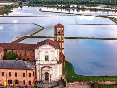Aerial view of the historic abbey rising majestically amidst a patchwork of flooded rice paddies, a serene tapestry of water and sky, Vercelli, Italy.