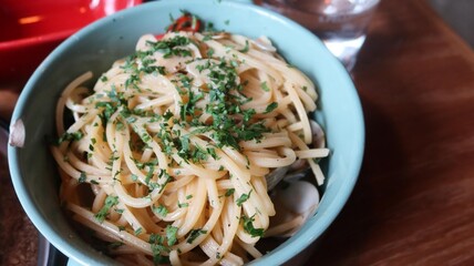 close up of spaghetti alle vongole with clams and herbs in a light blue plate on a wooden table with copy space
