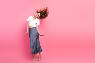 Fashionable young woman with long brown hair and trendy outfit posing on vibrant pink background...